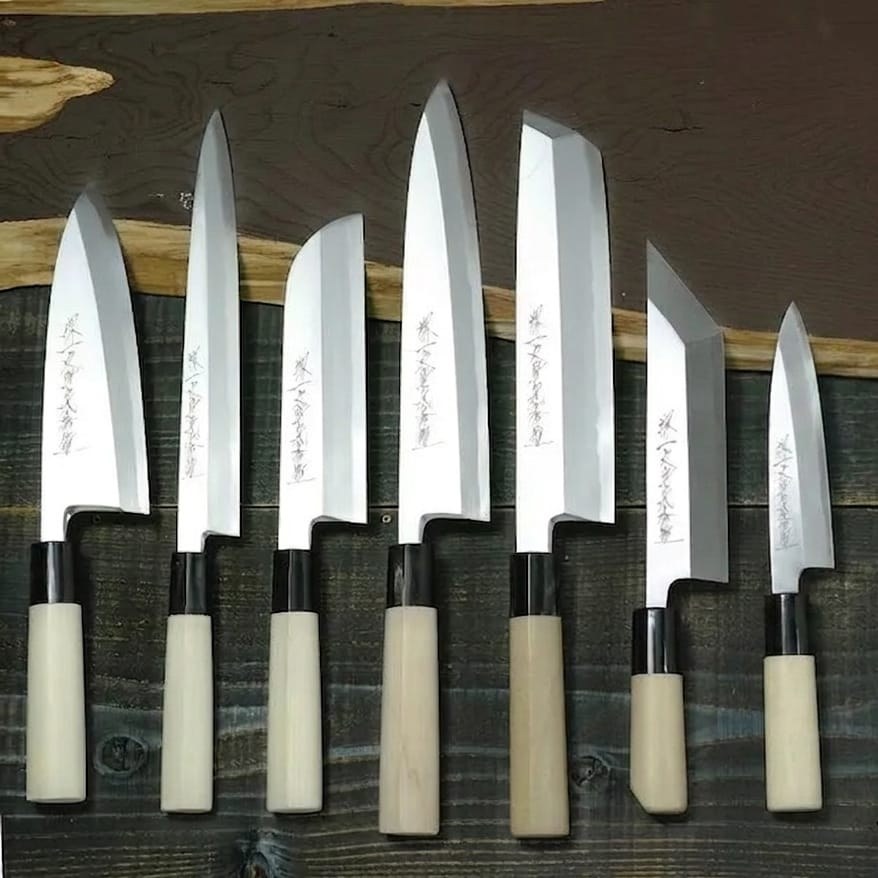 Diversi coltelli da cucina giapponesi allineati, con lame e manici tradizionali