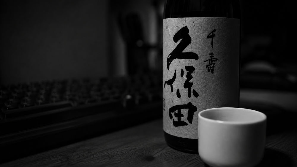 Bottiglia di nihonshu Kubota e ochoko bianca, foto in bianco e nero.